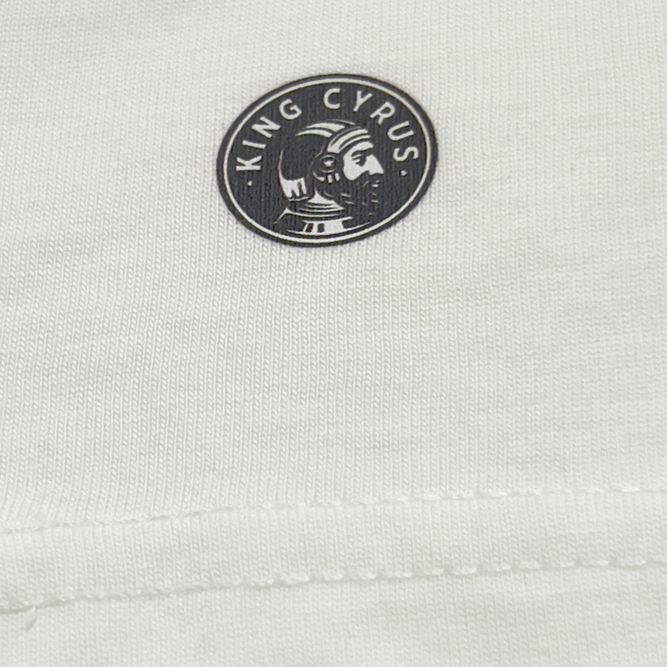 Close-up of King Cyrus logo printed on bottom left of back of white t-shirt