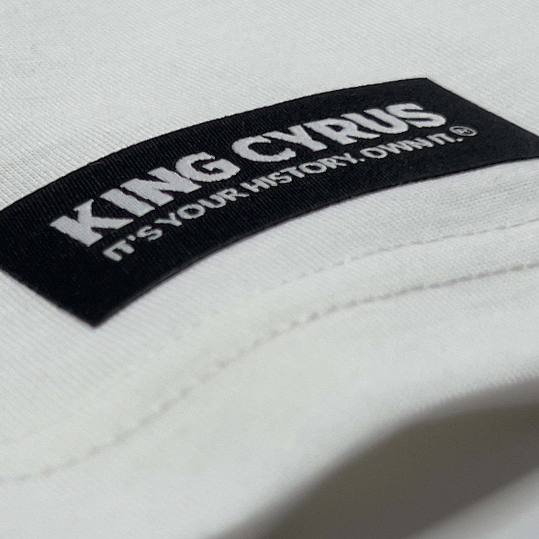 King Cyrus woven tag with tagline 'It’s Your History. Own It.' on front hem of white tee